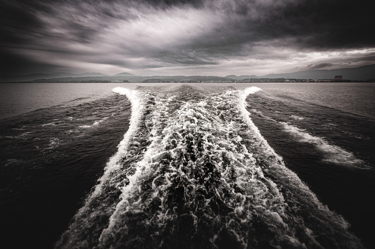 Sillage d'un bateau sur une étendue d'eau sombre sous un ciel nuageux.
