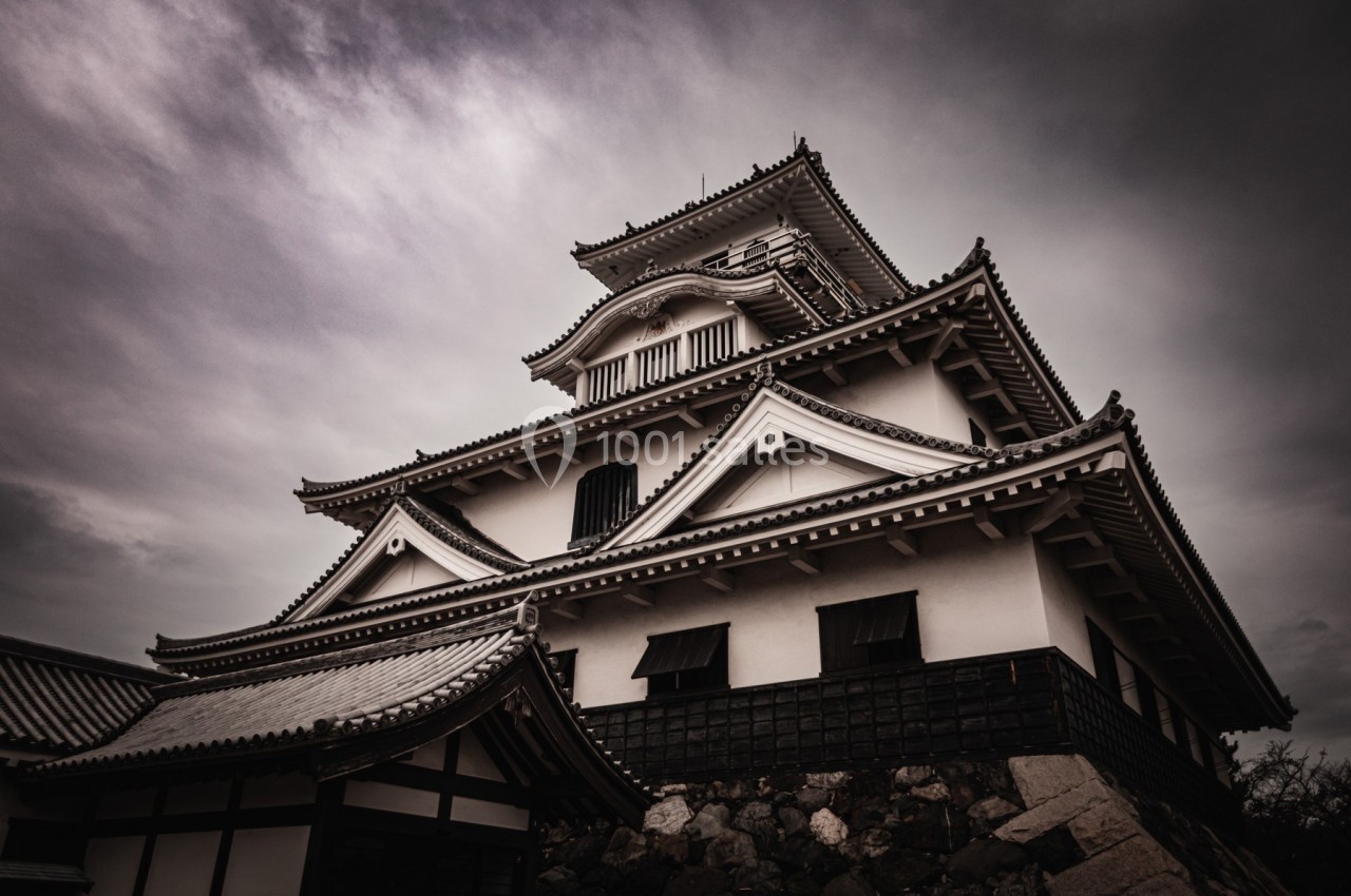 Château japonais traditionnel sous un ciel nuageux, avec des détails architecturaux en bois et en pierre.