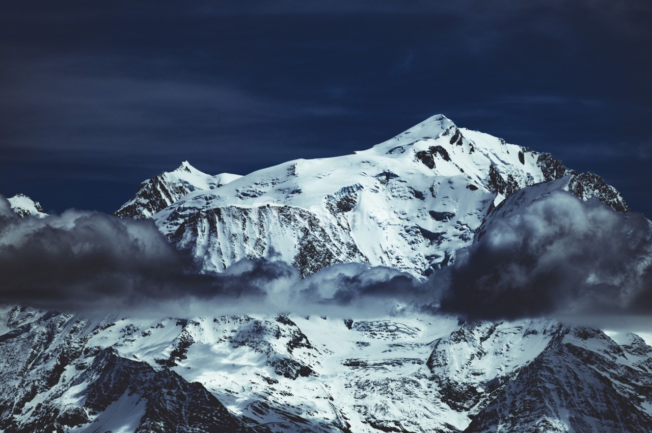 Montagne enneigée sous un ciel sombre, partiellement voilée par des nuages bas.