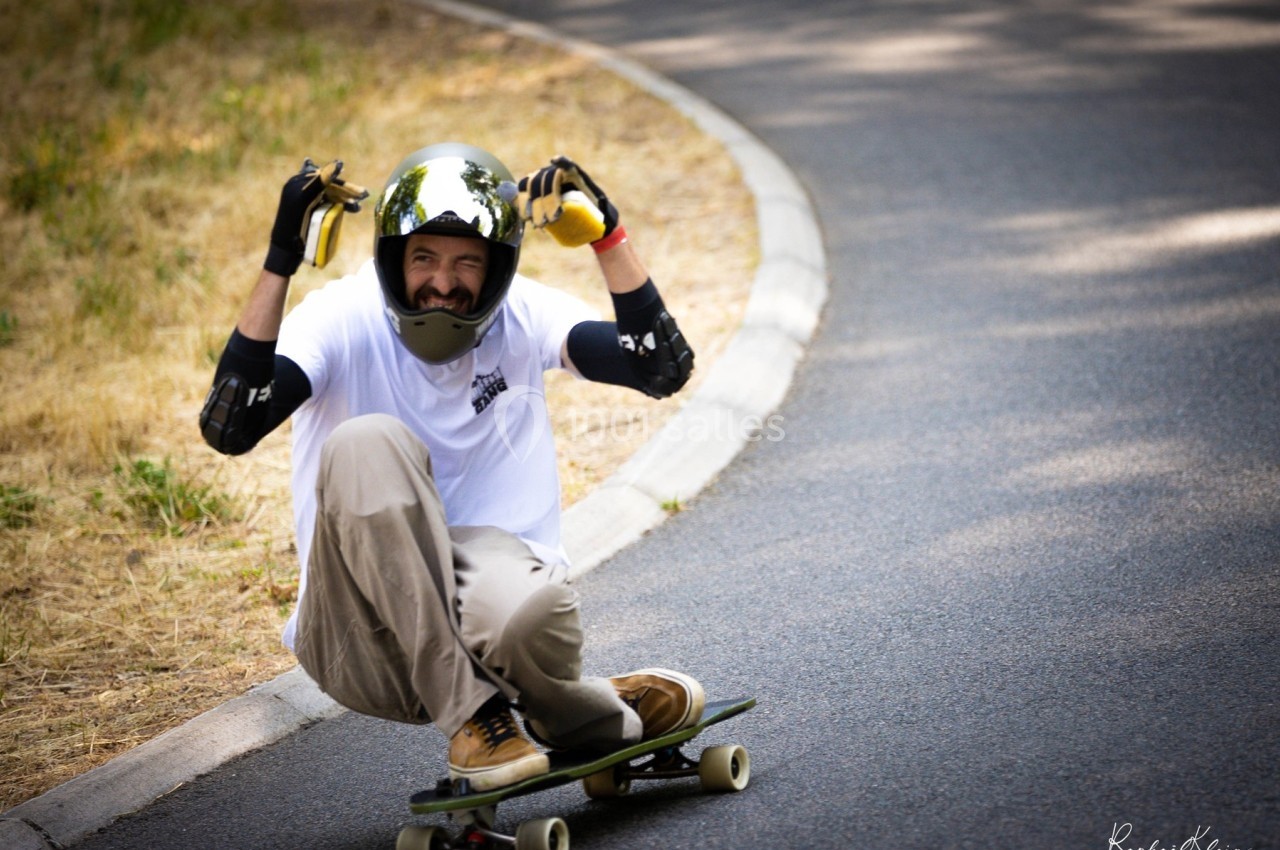 Un skateur portant un casque et des protections descend une route en longboard, adoptant une posture accroupie.