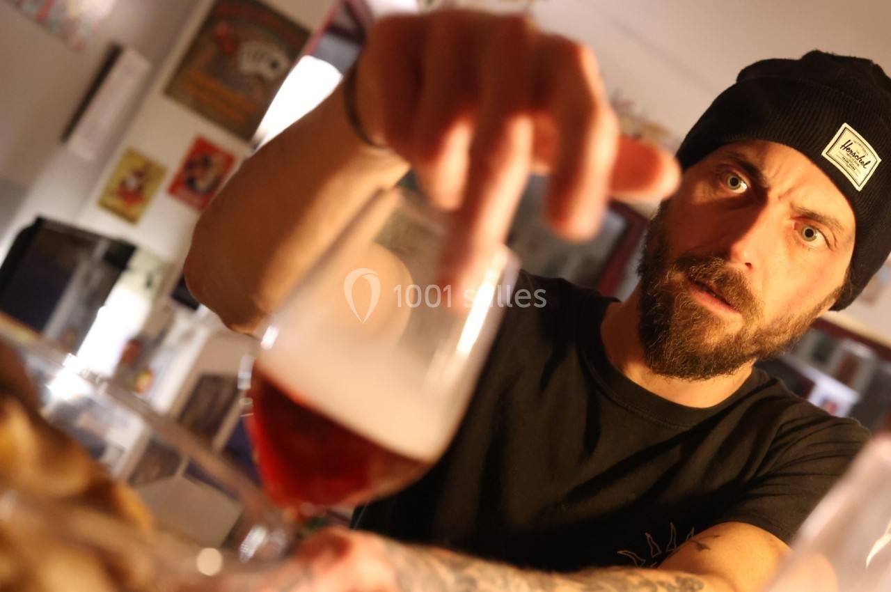 Un homme portant un bonnet noir tend la main vers un verre de bière dans un intérieur éclairé.