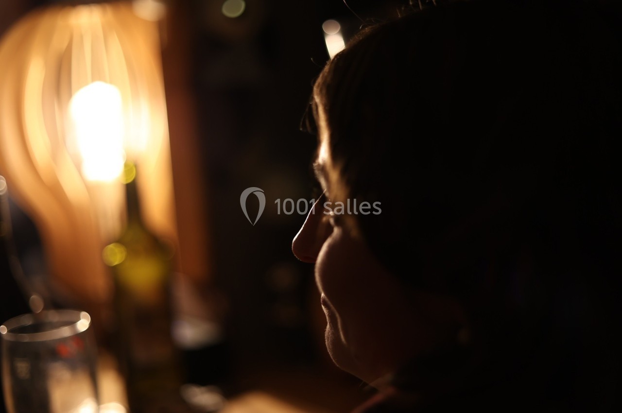 Femme de profil dans une ambiance tamisée, éclairée par une lampe et entourée d'objets flous en arrière-plan.