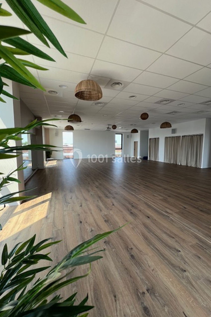 Salle spacieuse avec parquet en bois, plafond à dalles blanches et suspensions en osier, éclairée par de grandes fenêtres.