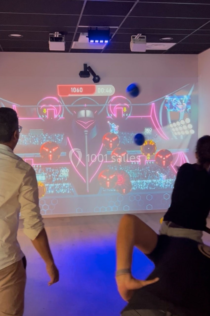Deux personnes jouent à un jeu interactif projeté sur un mur, lançant des balles vers des cibles lumineuses.
