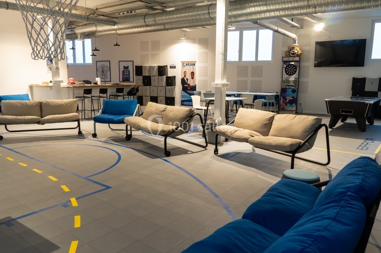 Espace de détente avec canapés, baby-foot, cible de fléchettes et coin cuisine dans un environnement lumineux.