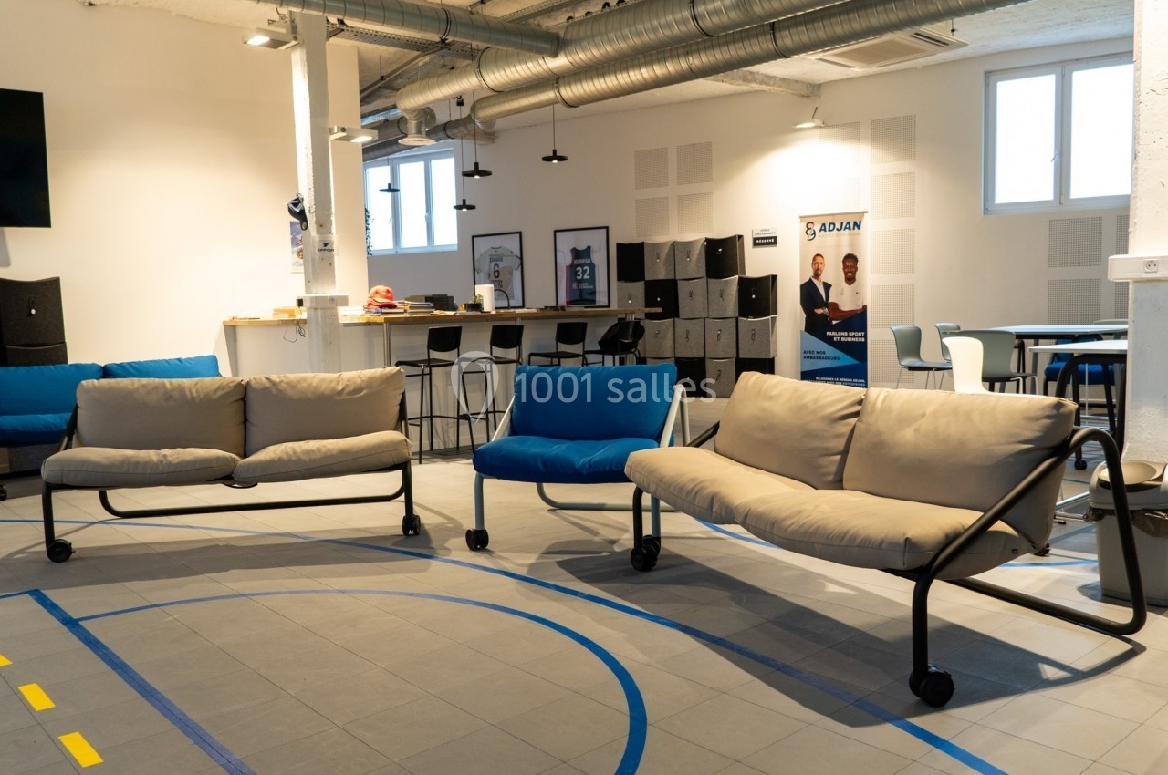 Espace intérieur lumineux avec canapés sur roulettes, tables hautes, casiers et affiches dans un cadre moderne.