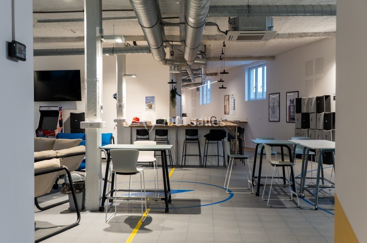 Espace de coworking moderne avec tables, chaises, canapés et décor industriel.