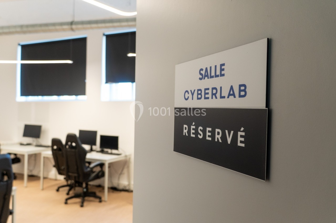 Panneau indiquant ’Salle Cyberlab - Réservé’ devant une pièce équipée de bureaux et d'ordinateurs.