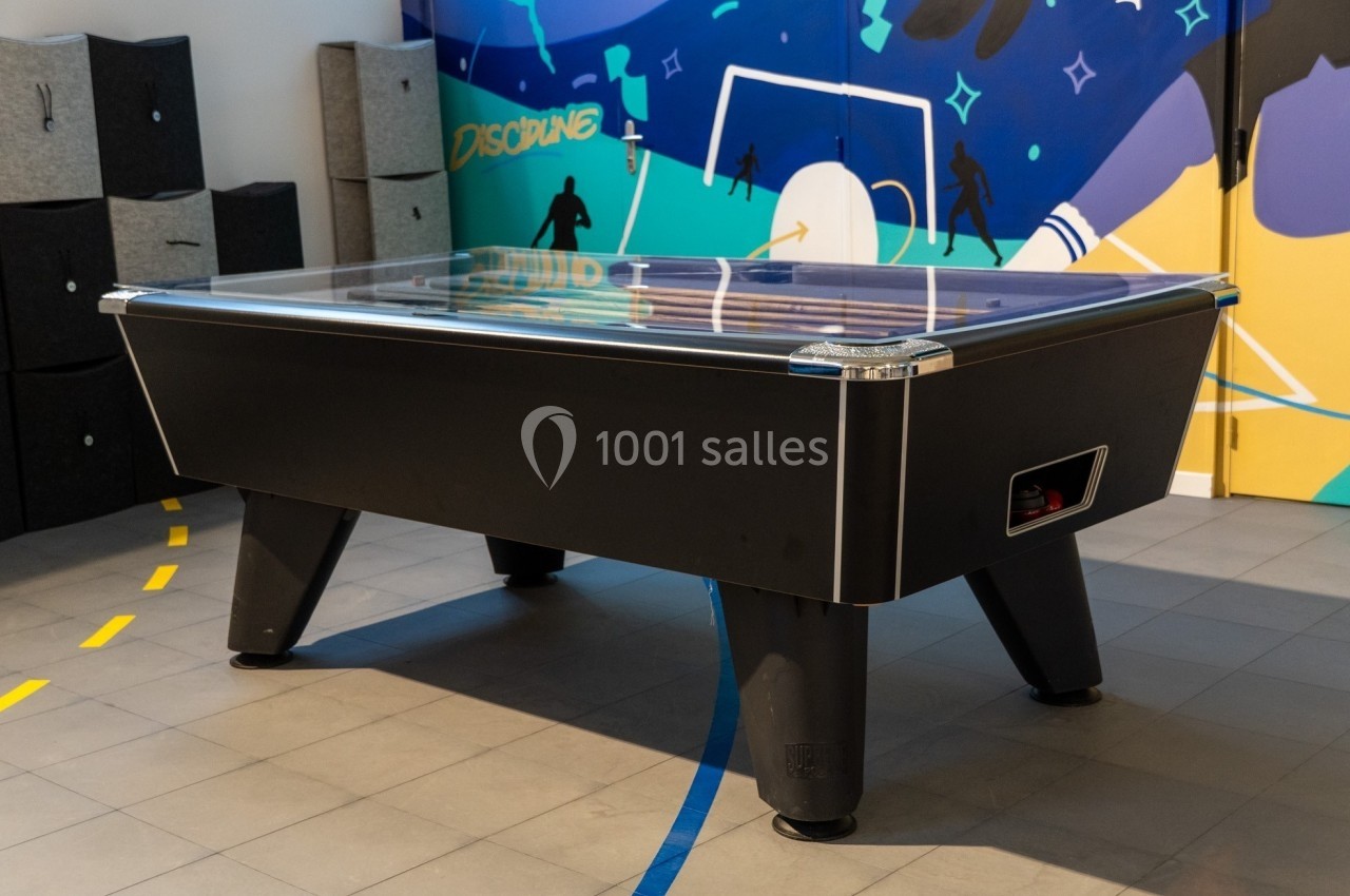 Table de hockey sur air noire dans une salle de loisirs avec un mur coloré en arrière-plan.