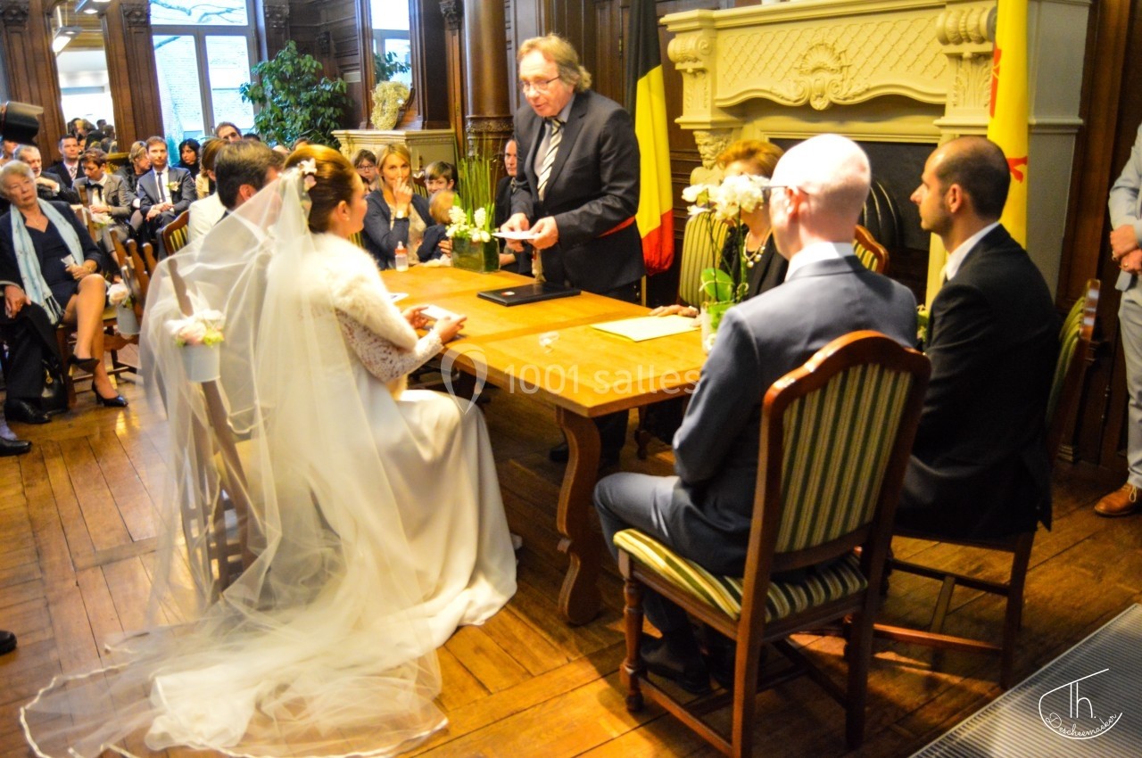 Un couple assis face à un officier célébrant une cérémonie de mariage dans une salle ornée de boiseries.