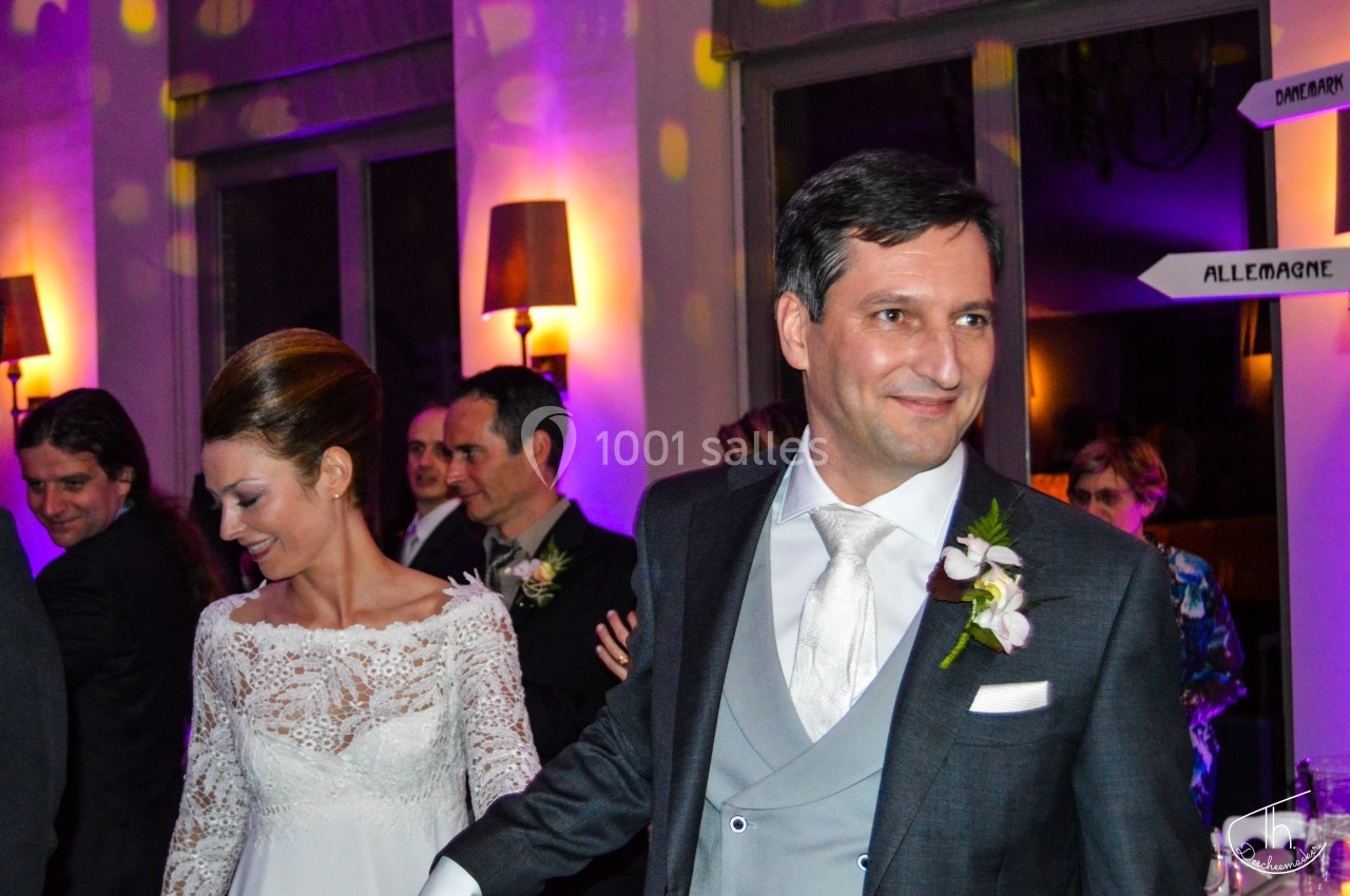 Un couple en tenue de mariage danse dans une salle éclairée avec des invités en arrière-plan.