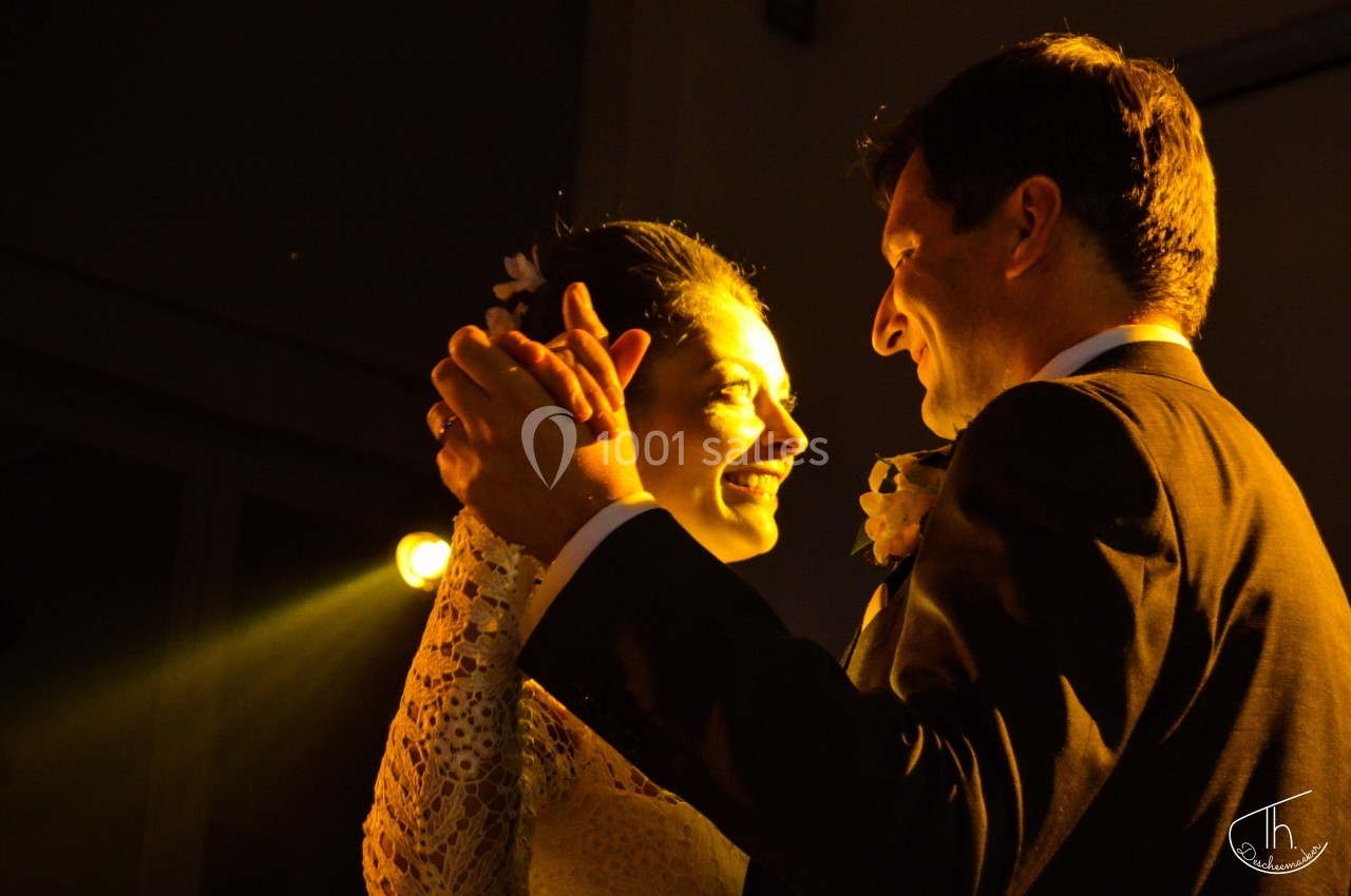 Un couple danse sous une lumière chaude, la mariée souriant en regardant le marié.