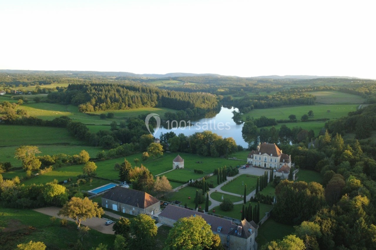 Vue aérienne d'un domaine avec un château, des jardins aménagés, une piscine et un lac entouré de forêts et prairies.