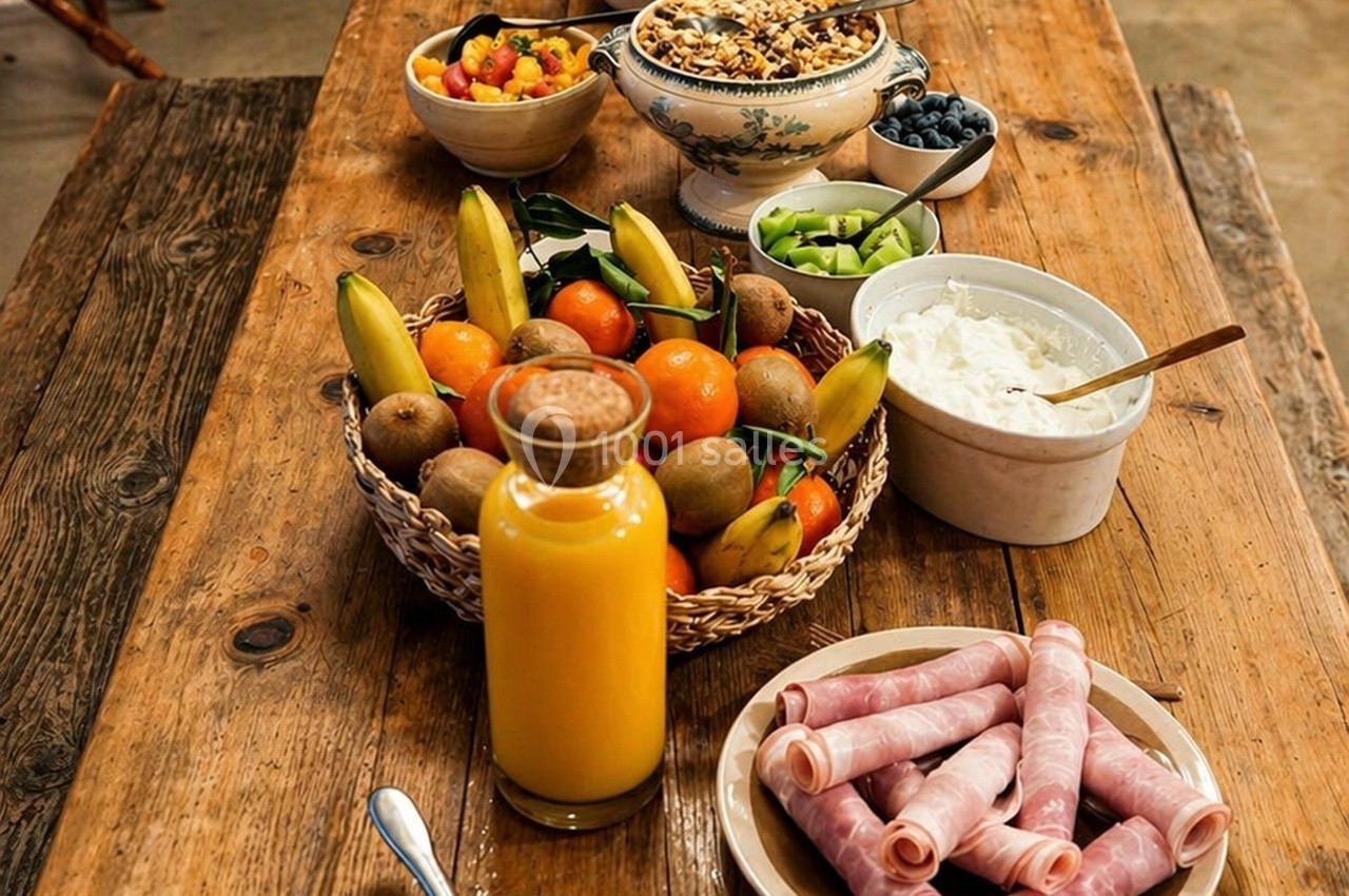 Petit-déjeuner sur une table en bois avec fruits, yaourt, céréales, jus d'orange et roulés de jambon.