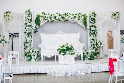Décor de mariage avec canapé blanc, table assortie et fleurs blanches et vertes sur une estrade ornée.