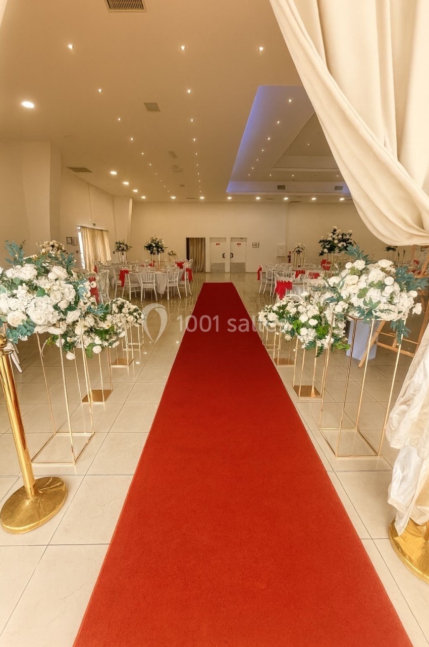 Allée centrale avec tapis rouge menant à une salle de réception décorée de fleurs blanches et de tables dressées.