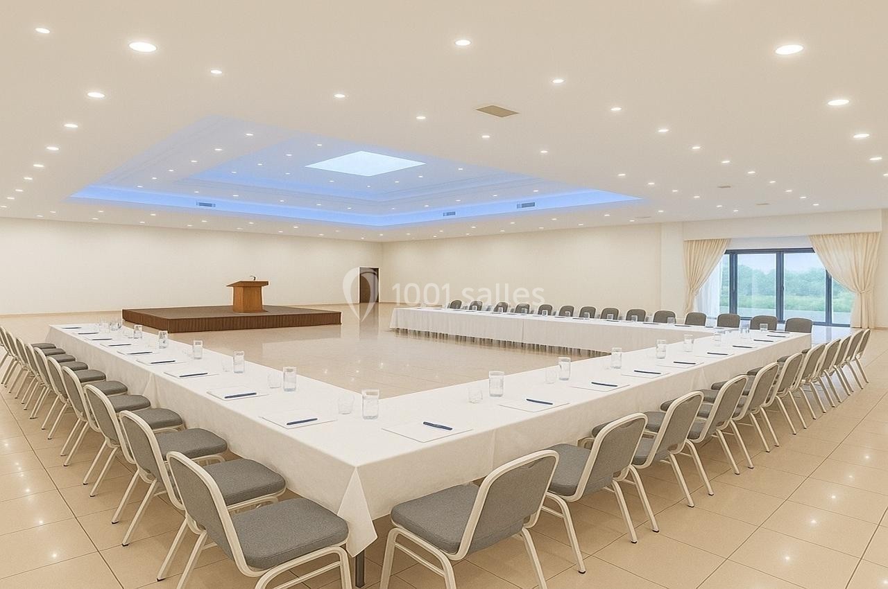 Salle de conférence lumineuse avec tables disposées en U, chaises alignées et un podium sur une estrade.