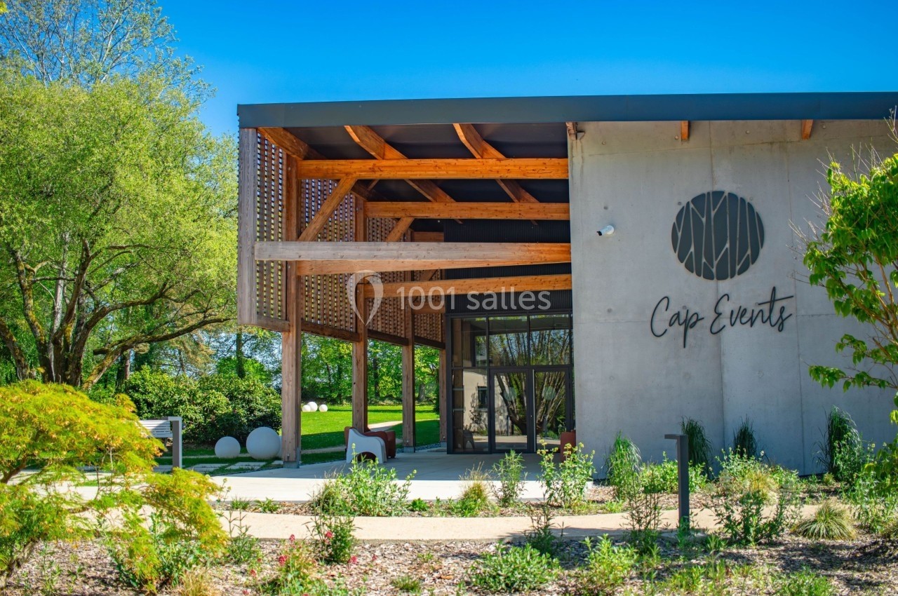 Façade d'un bâtiment moderne avec structure en bois, jardin paysager et logo ’Cap Events’ sur le mur.