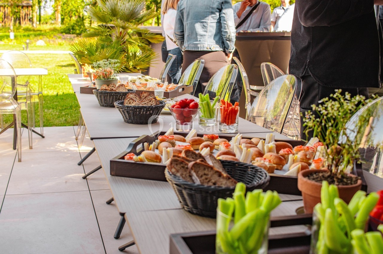 Buffet en extérieur avec tables garnies de pains, légumes, dips et amuse-bouches, entouré de convives debout.
