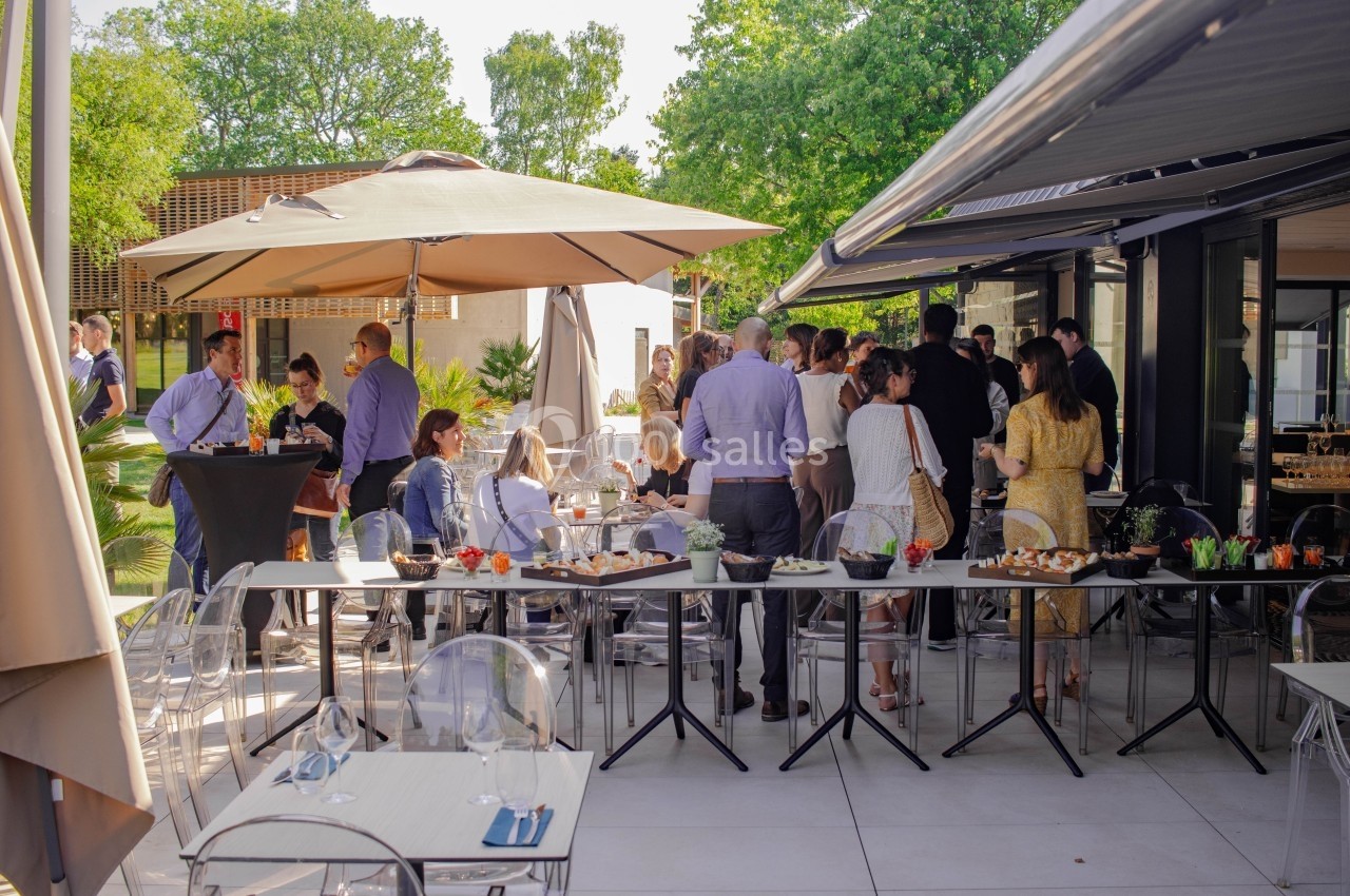 Groupe de personnes rassemblées sur une terrasse ensoleillée, autour de tables avec des plats et boissons.