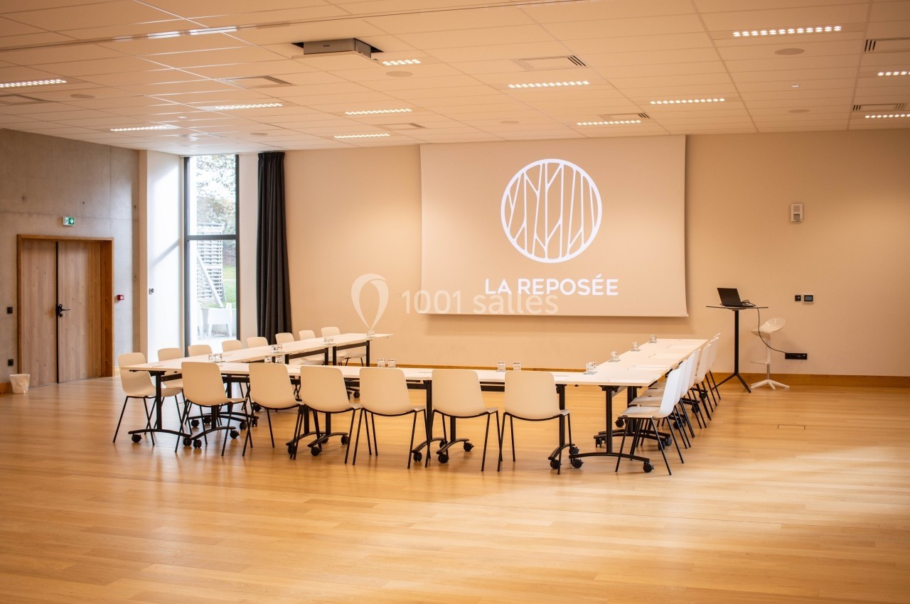 Salle de réunion lumineuse avec tables disposées en U, chaises blanches et écran de projection affichant ’La Reposée’.