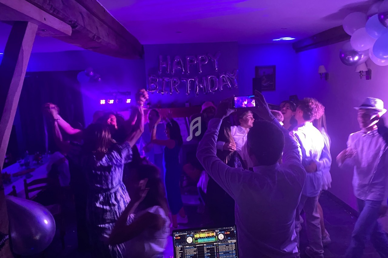 Groupe de personnes dansant lors d'une fête d'anniversaire avec des lumières colorées et une décoration ’Happy Birthday’.