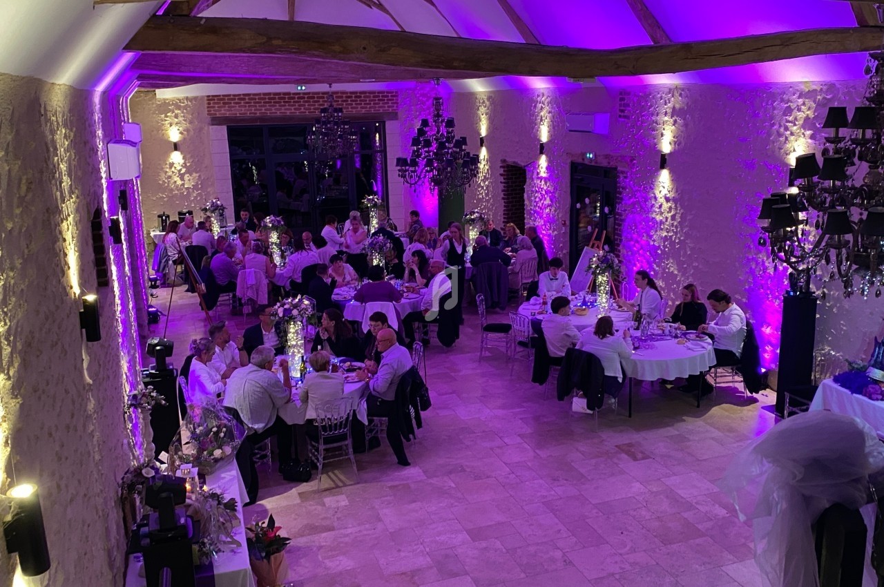 Salle de réception avec des invités assis à des tables rondes, éclairée par une lumière violette et des lustres noirs.
