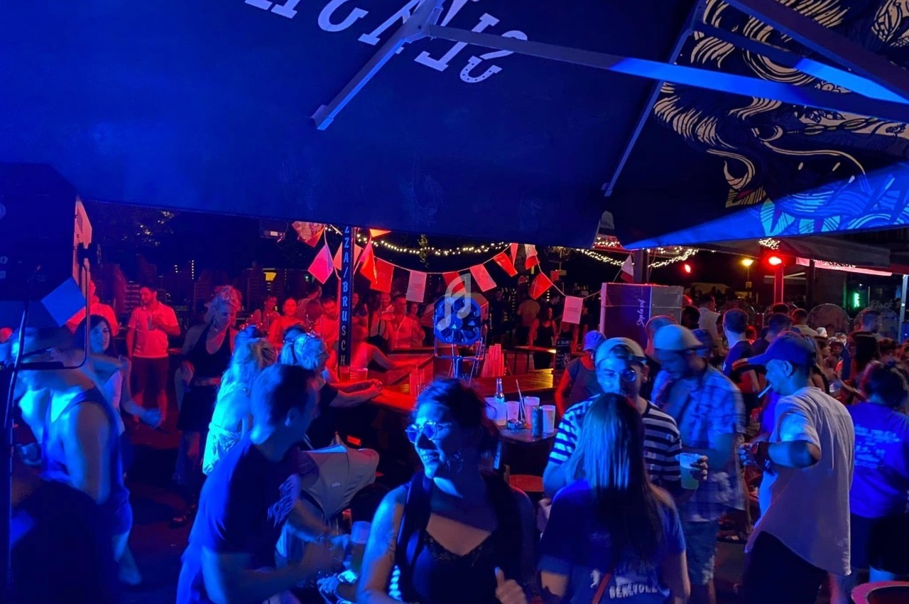 Groupe de personnes dansant et socialisant sous des lumières colorées dans un espace extérieur festif.