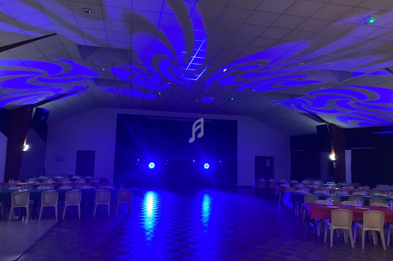Salle de réception avec tables dressées et éclairage bleu projeté au plafond et sur le sol.