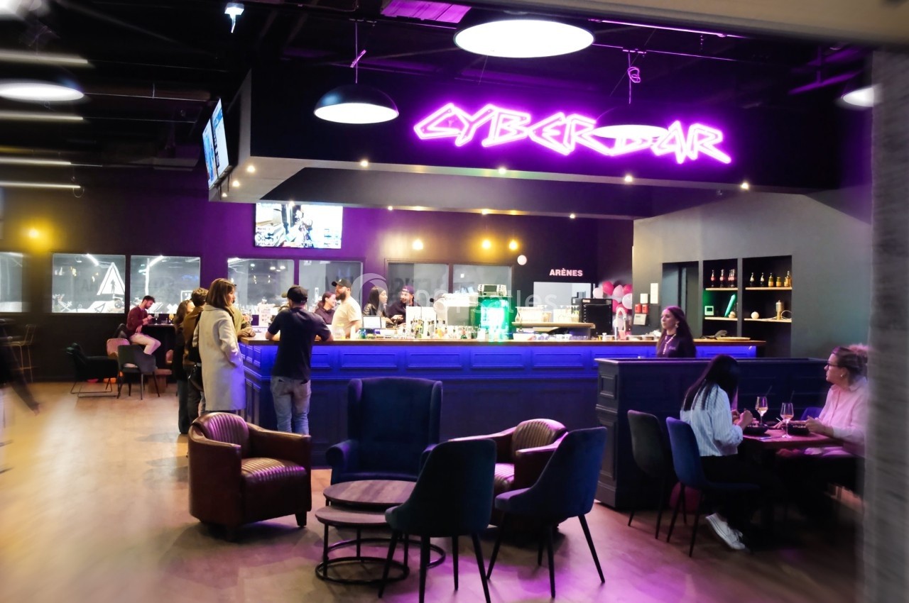 Espace intérieur d'un bar moderne avec éclairage néon, clients assis et debout autour du comptoir et des tables.