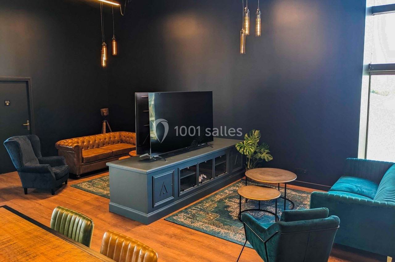 Salon moderne avec murs sombres, canapé en cuir, fauteuils, tapis coloré, meuble TV et éclairage suspendu.