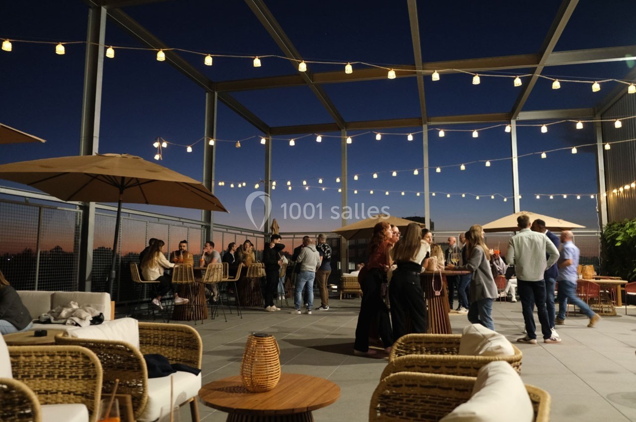 Terrasse extérieure en soirée avec des groupes de personnes discutant sous des guirlandes lumineuses.