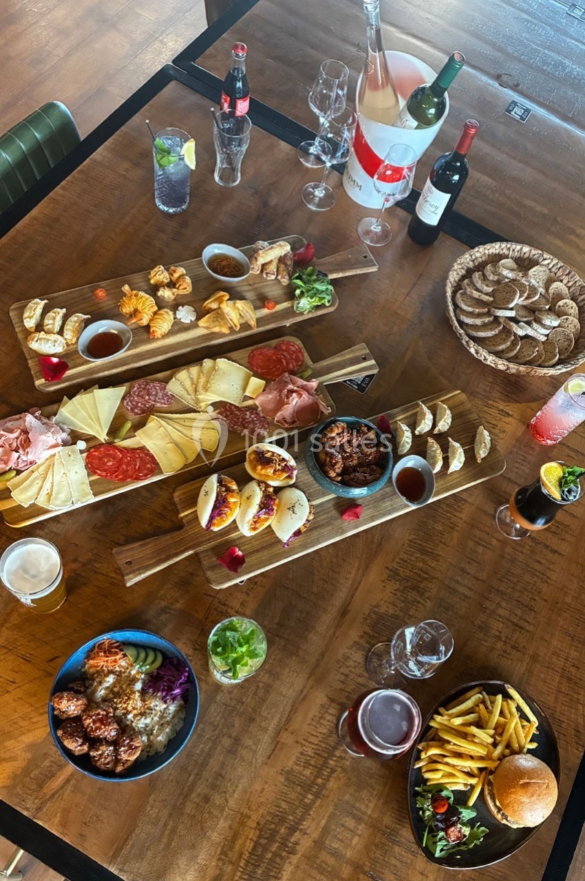 Table en bois garnie de planches apéritives variées, boissons, pain, frites et plats individuels.