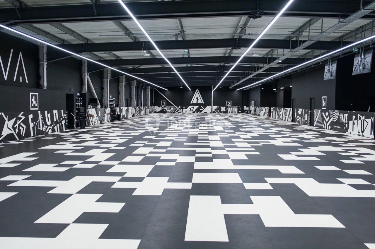 Salle intérieure spacieuse avec un sol noir et blanc à motifs géométriques et des murs décorés de graphismes abstraits.