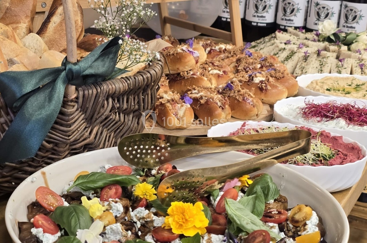 Buffet avec salades colorées, pains variés, fleurs comestibles et bouteilles de vin en arrière-plan.