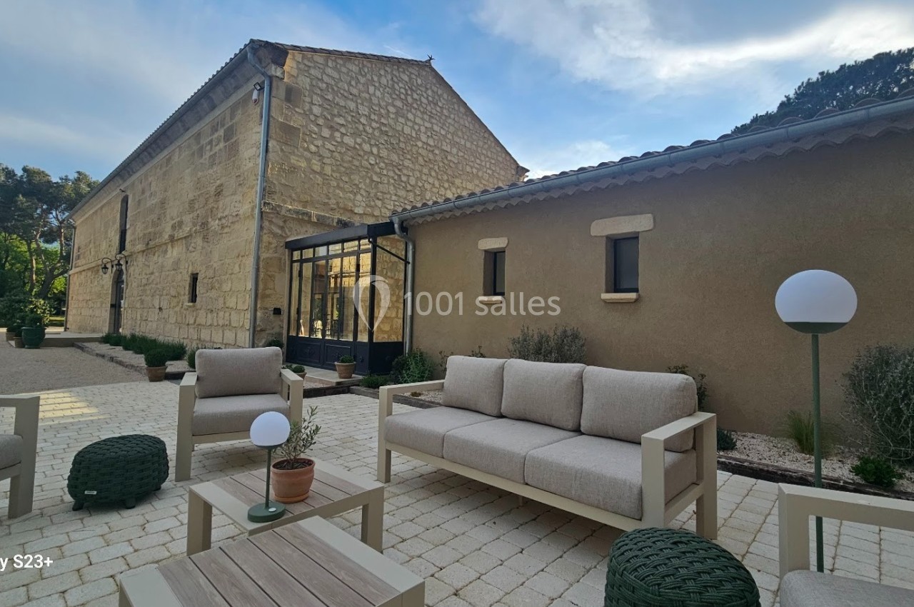 Mobilier de jardin beige et vert disposé sur une terrasse pavée, devant une maison en pierre avec véranda.