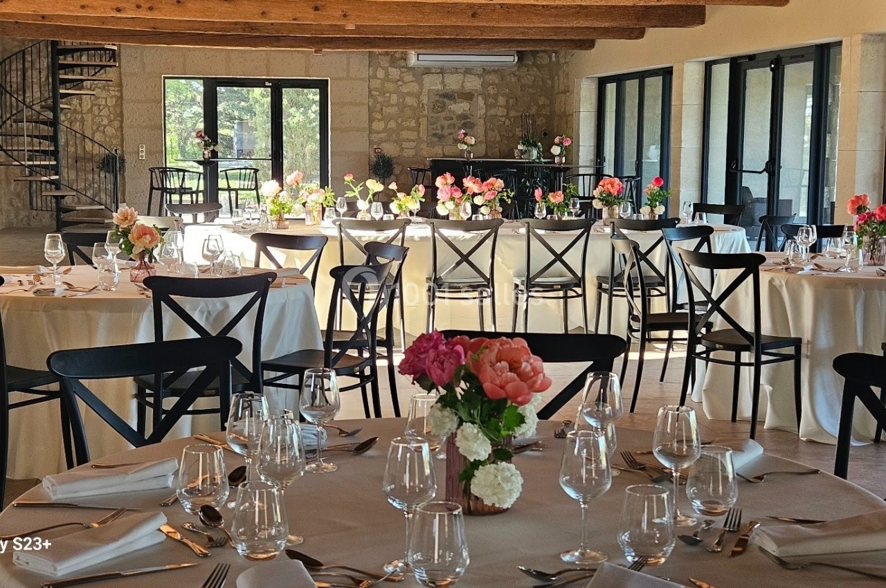 Salle de réception lumineuse avec tables rondes et rectangulaires décorées de fleurs et dressées pour un repas.