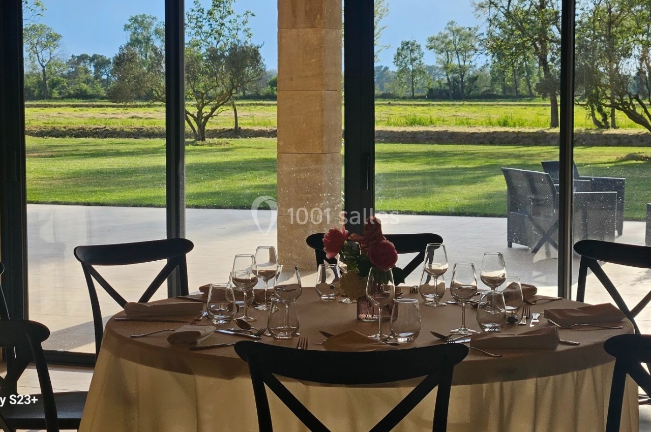 Table dressée avec vaisselle et fleurs, placée près de grandes baies vitrées donnant sur un jardin ensoleillé.