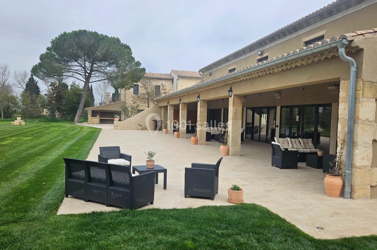 Terrasse spacieuse avec mobilier d'extérieur, bordée de pelouse et attenante à une grande maison en pierre.