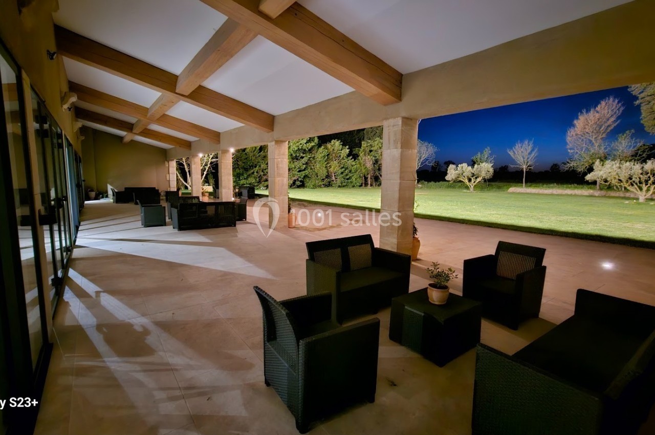 Terrasse couverte avec mobilier en rotin, vue sur un jardin éclairé et des arbres sous un ciel nocturne.