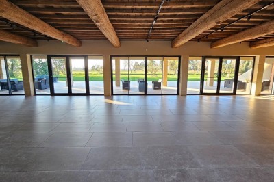 Bâtisse en pierre avec une verrière, entourée d'une cour pavée et d'espaces verts sous un ciel dégagé.