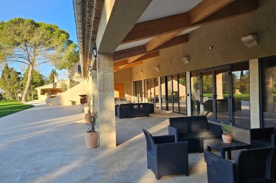 Bâtisse en pierre avec une verrière, entourée d'une cour pavée et d'espaces verts sous un ciel dégagé.