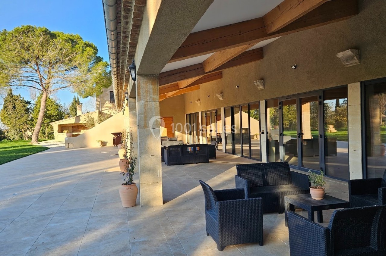 Terrasse spacieuse avec mobilier en rotin, grandes baies vitrées et vue sur un jardin arboré par temps ensoleillé.
