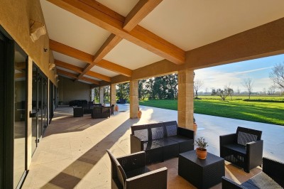 Bâtisse en pierre avec une verrière, entourée d'une cour pavée et d'espaces verts sous un ciel dégagé.