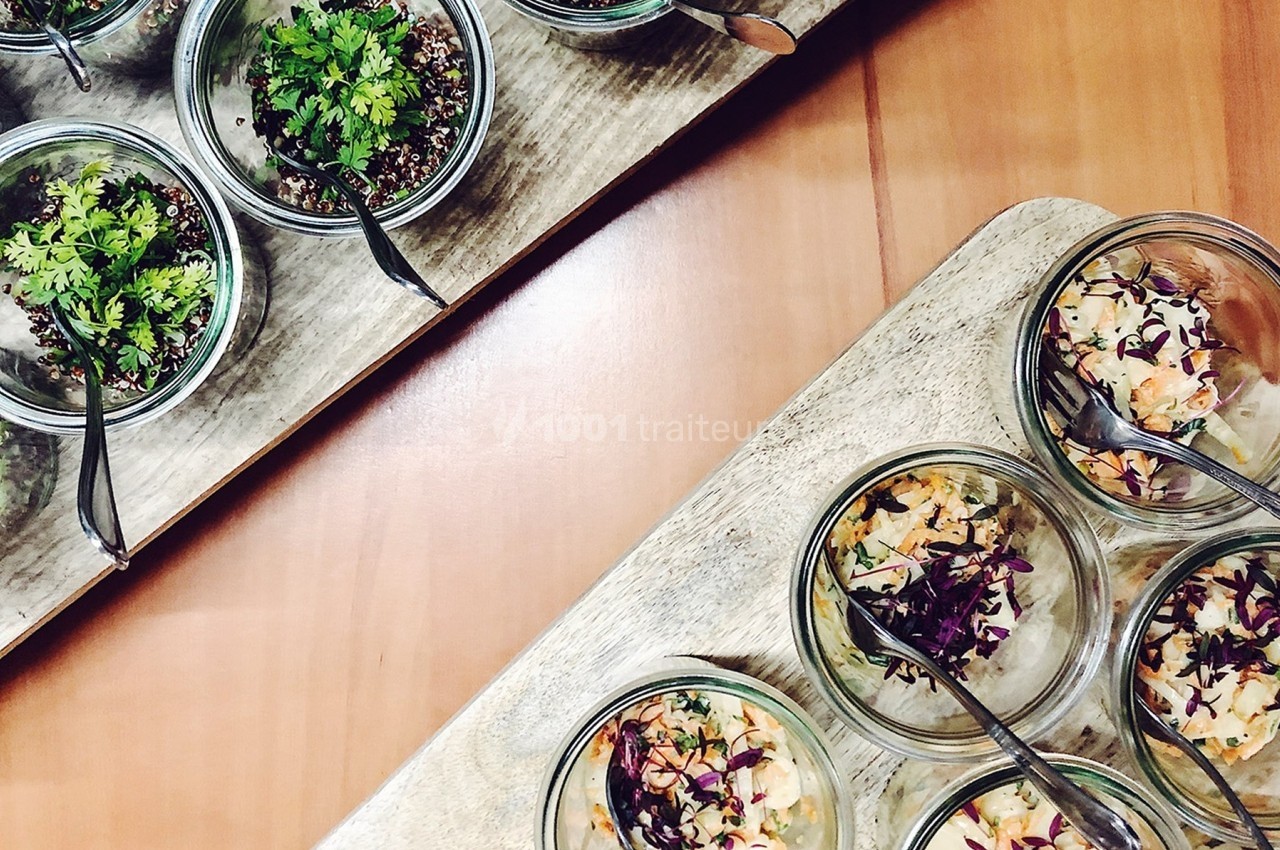 Des verrines garnies de salades colorées et herbes fraîches, présentées sur des plateaux en bois.