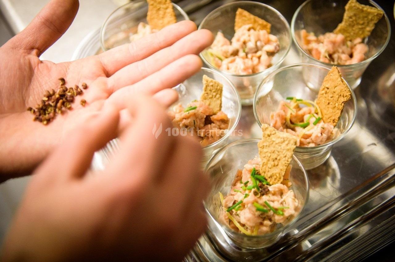 Préparation de verrines de tartare de poisson avec ajout de graines et décoration de crackers.