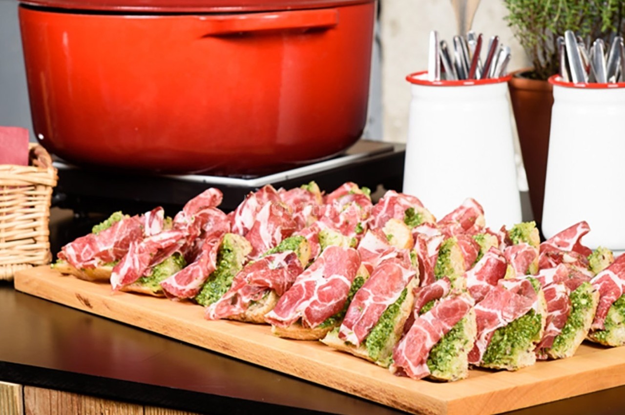 Plateau de tartines garnies de jambon cru et de pesto, posé sur une table devant une cocotte rouge.