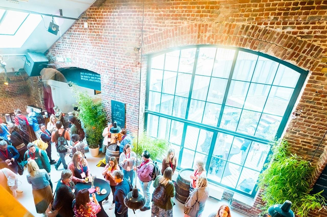 Des personnes discutent et échangent dans un espace lumineux avec de grandes fenêtres et des murs en briques.