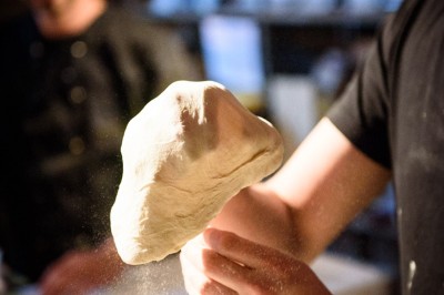 Miniature Traiteur Saint-Gilles (Bruxelles-Capitale) - La Tricoterie Traiteur #16 Une personne manipule une pâte à pizza en la faisant tourner dans un environnement de cuisine.