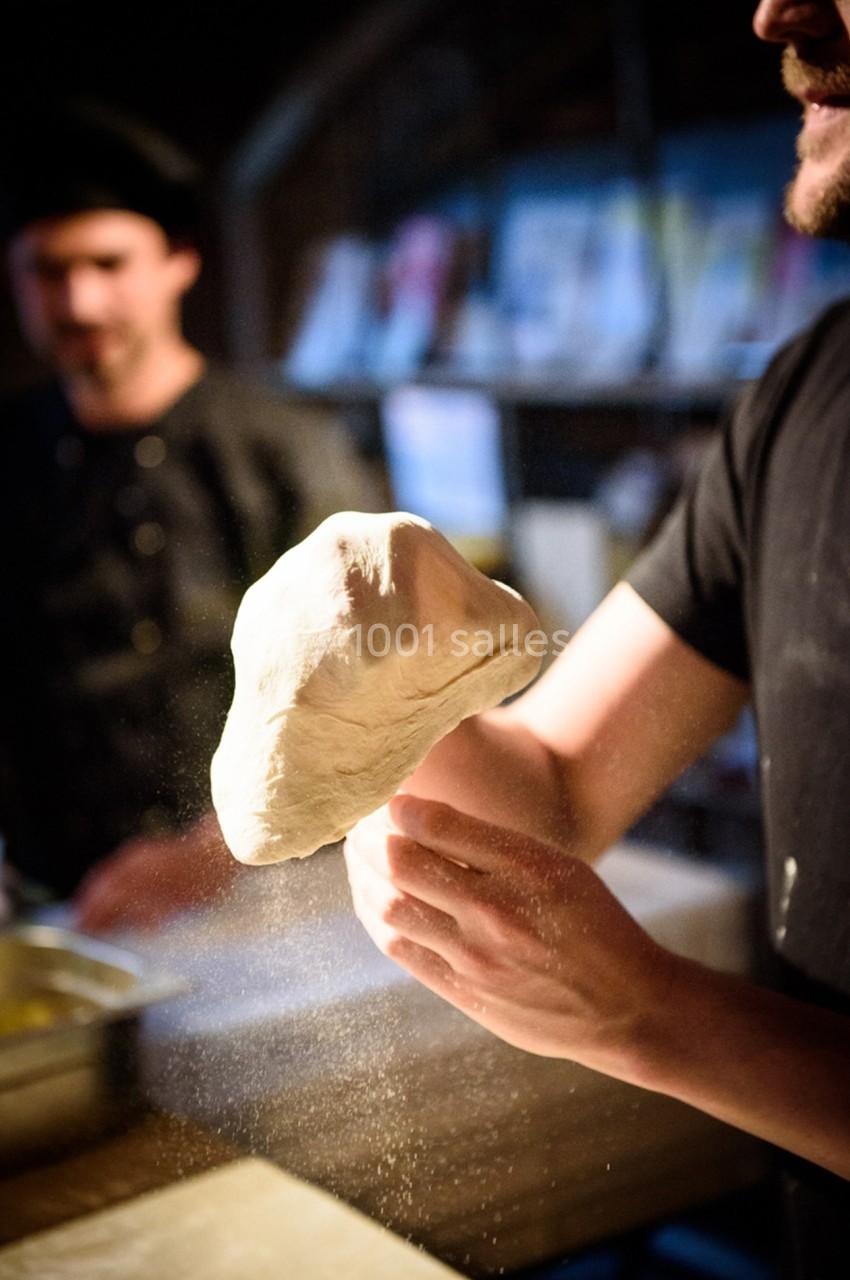 Une personne manipule une pâte à pizza en la faisant tourner dans un environnement de cuisine.